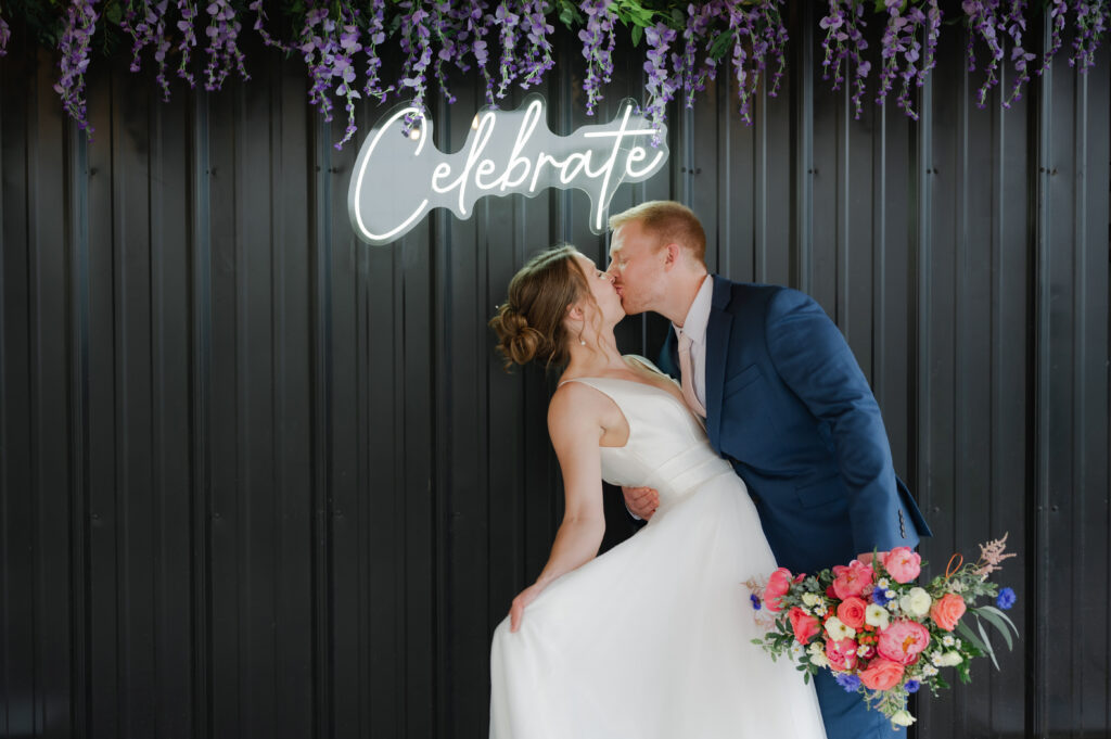 photo op with celebrate neon sign and purple wisteria against the black wall