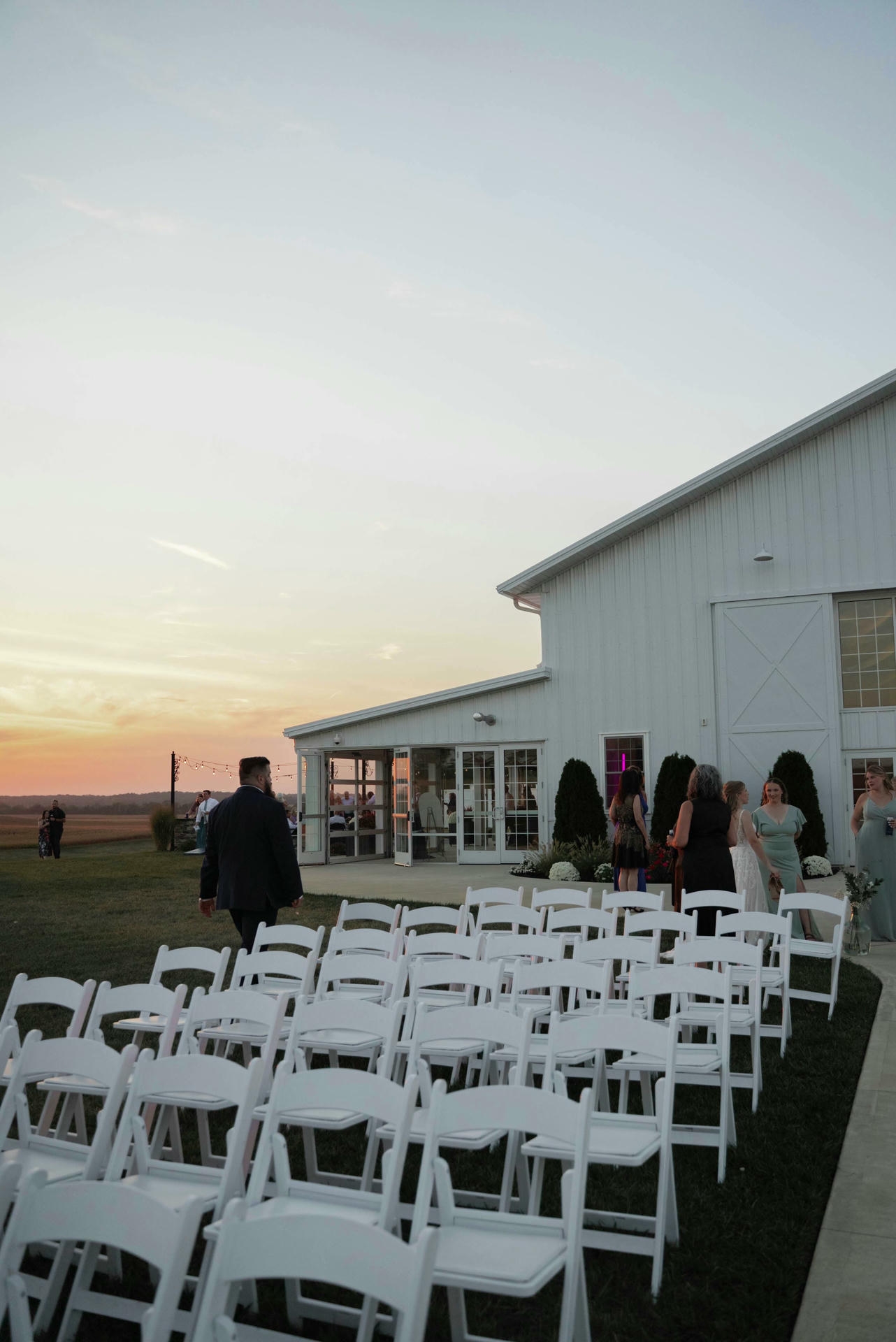 Outdoor central Iowa wedding venue with white barn, ceremony chairs, and a golden sunset over flat farmland