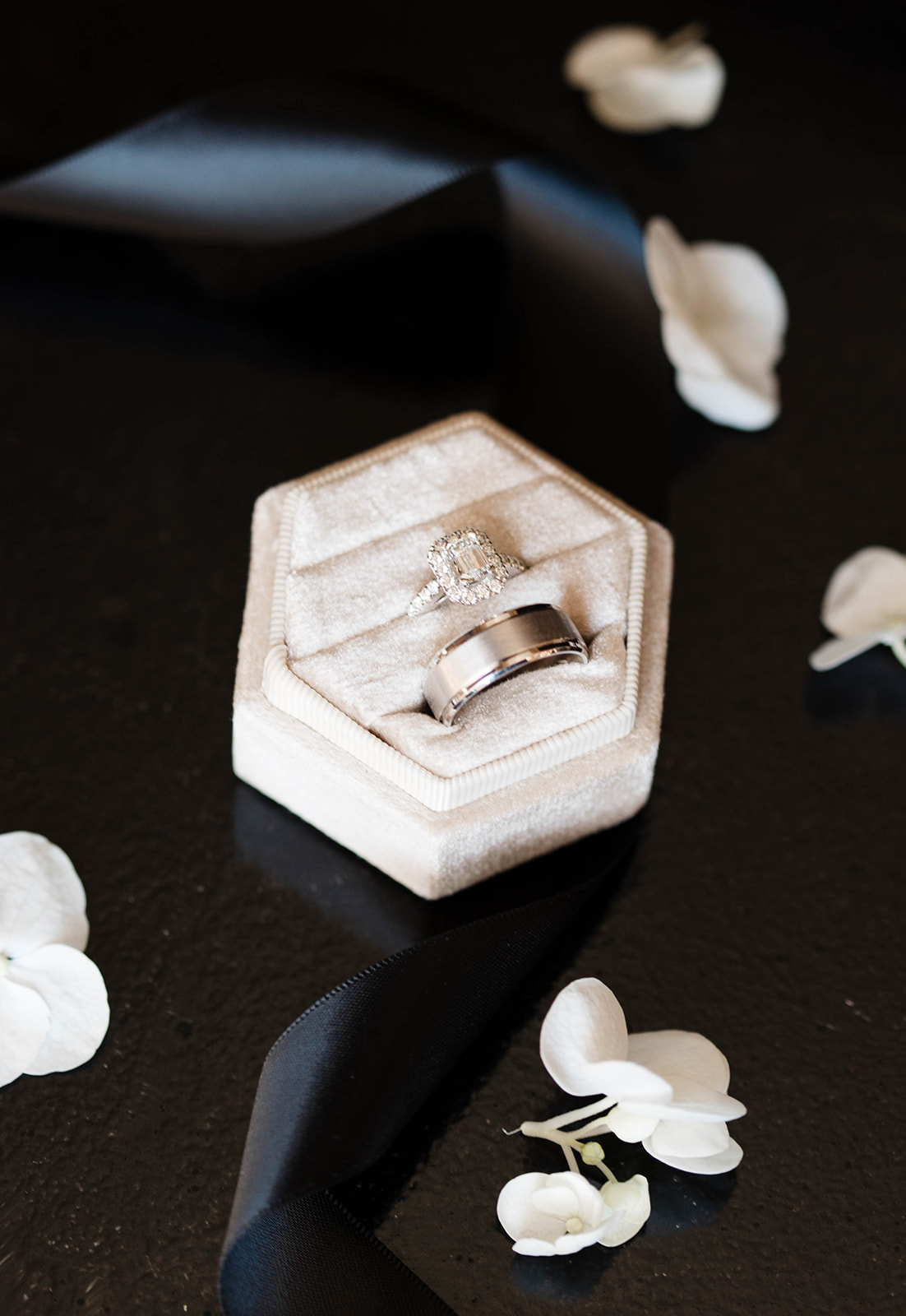Diamond engagement ring and wedding band in a velvet hexagon ring box surrounded by white flower petals