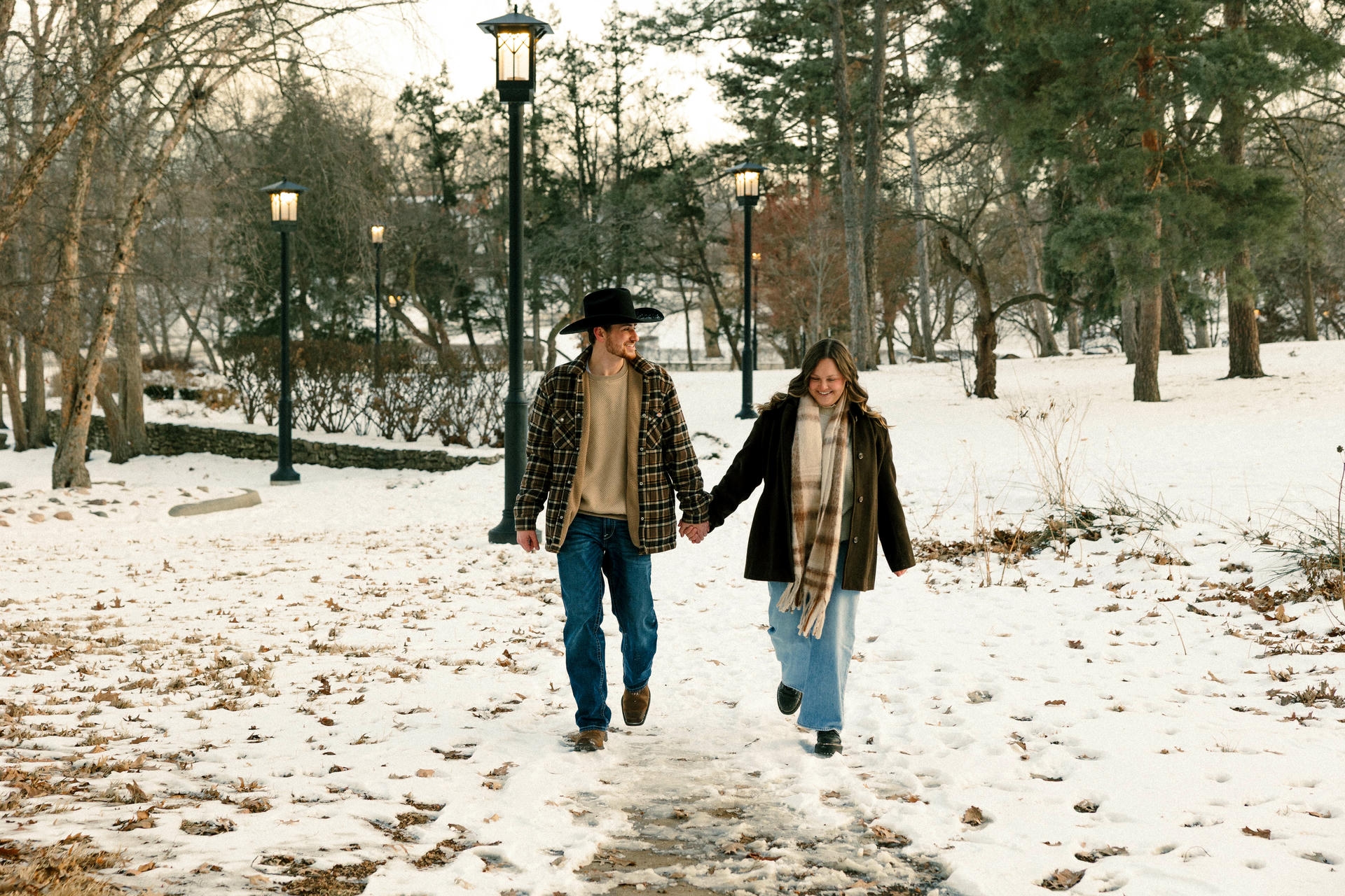 Couple holding hands and walking together on a snowy park path, pre-engagement photo in Iowa winter
