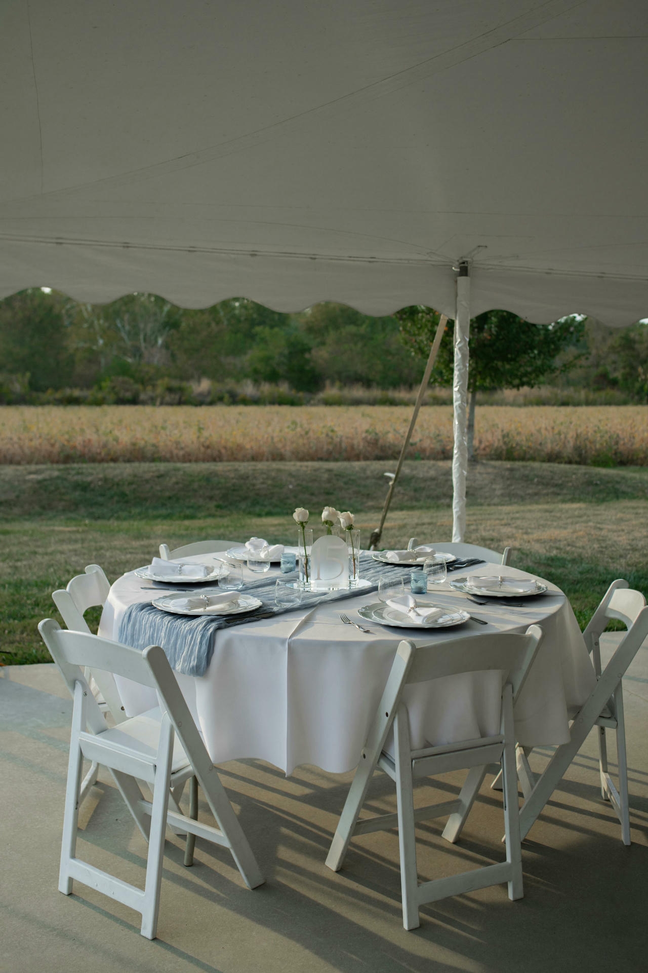 Outdoor Iowa wedding reception table set under a white tent with a field and trees in the background