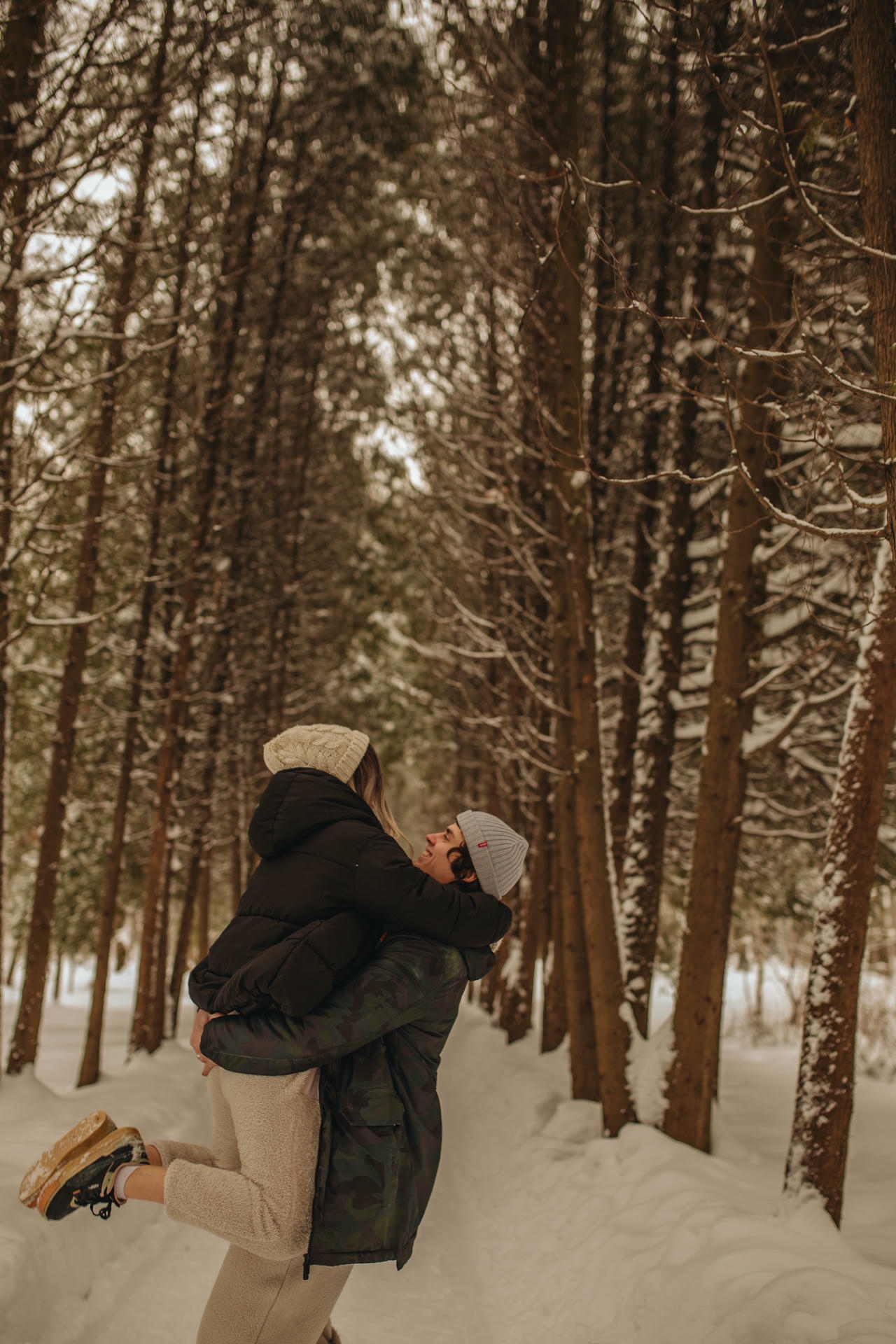 Couple laughing and embracing in a snowy winter forest, pre-engagement couple photo
