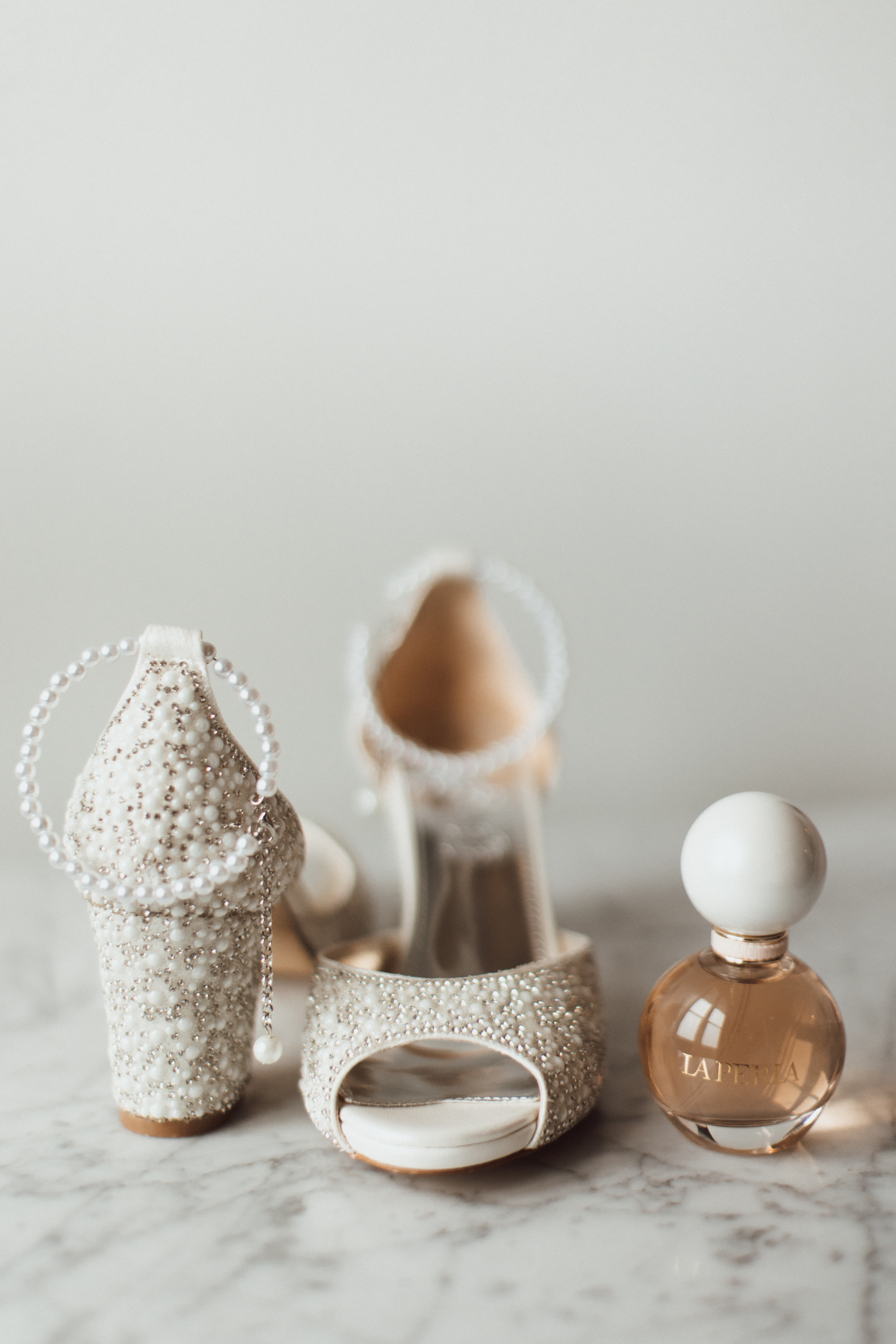 Pearl-embellished bridal heels and perfume bottle on a marble surface, wedding detail shot