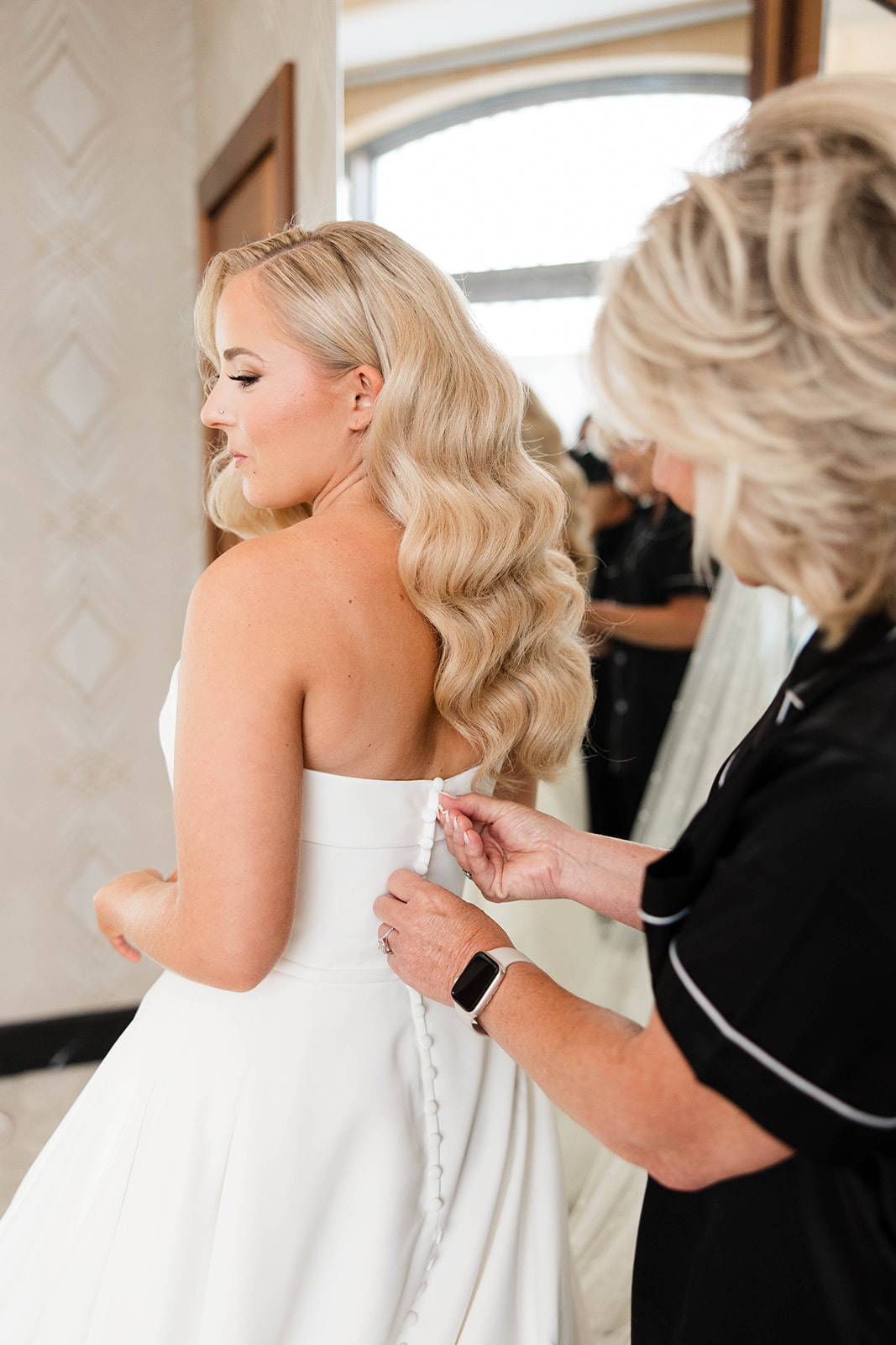 Bride having her wedding dress buttoned by a family member during wedding morning preparations, getting ready photo