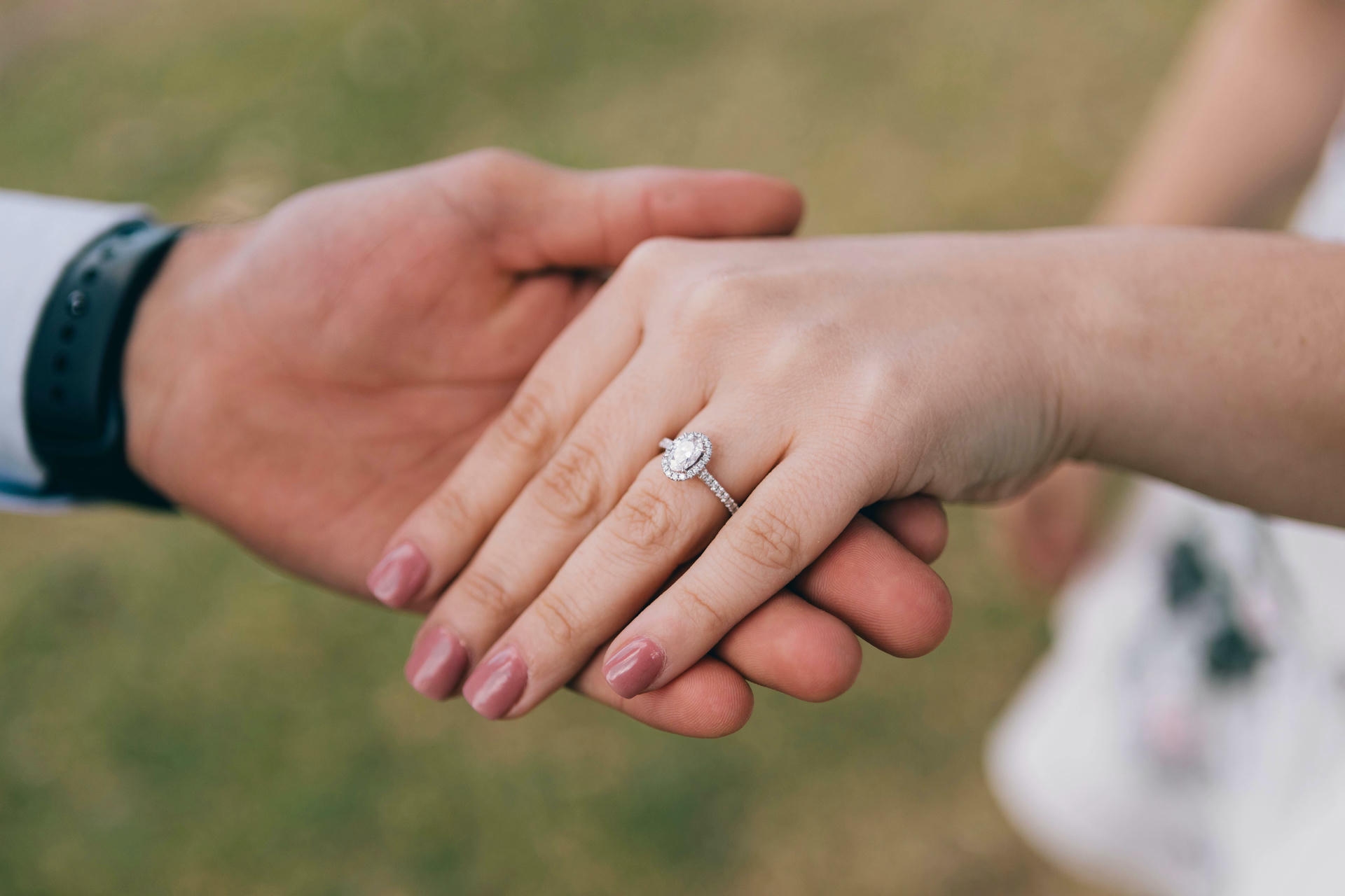 Close-up of a couple holding hands with a diamond engagement ring, pre-proposal wedding planning.