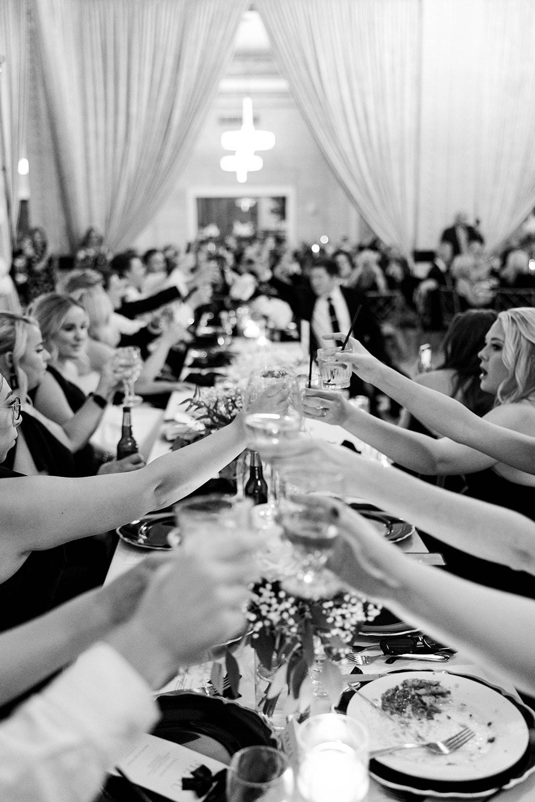 Wedding guests raising glasses in a toast at a full Iowa reception hall, black and white photo