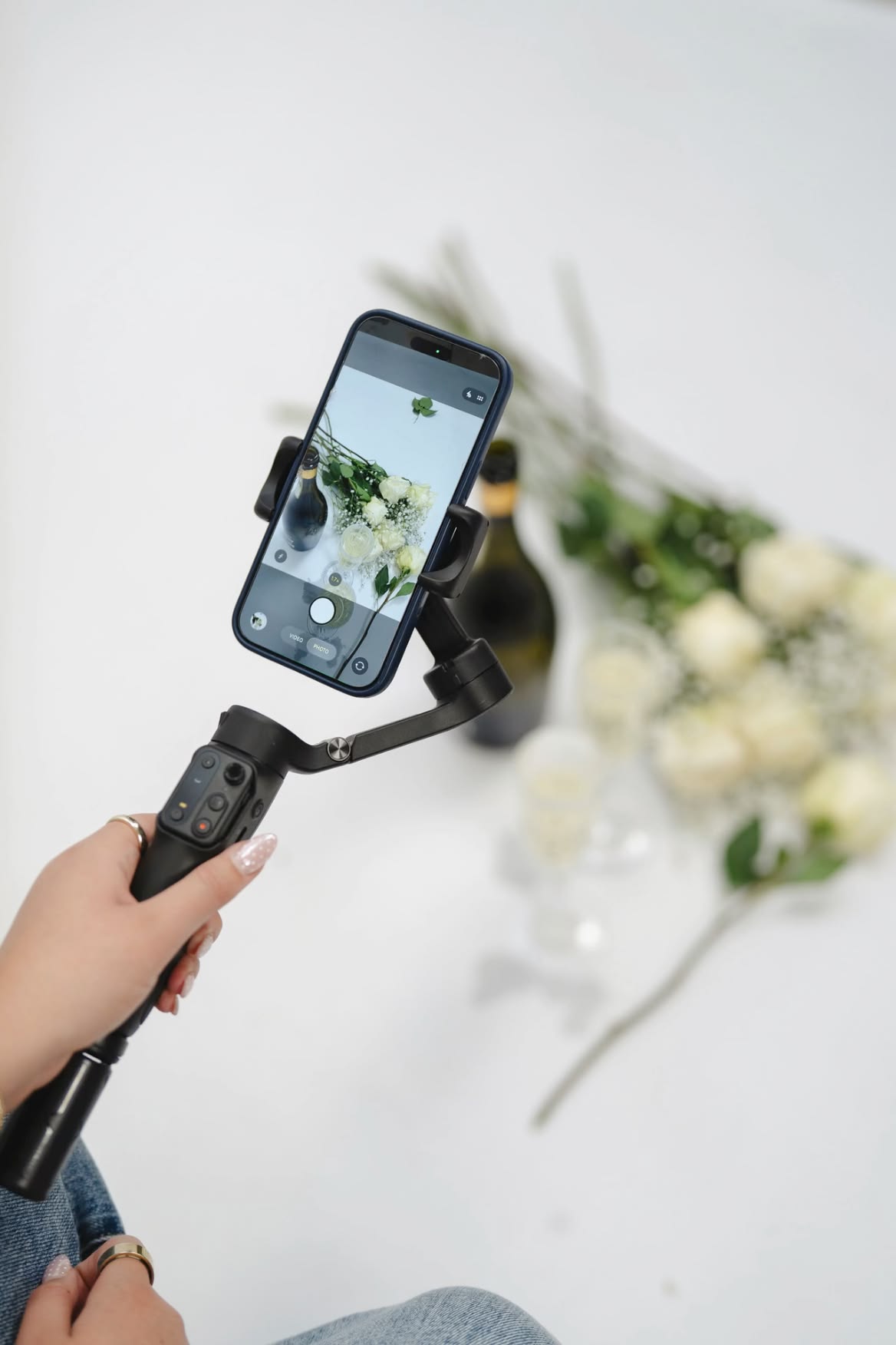 Wedding content creator filming with a phone gimbal near florals and champagne