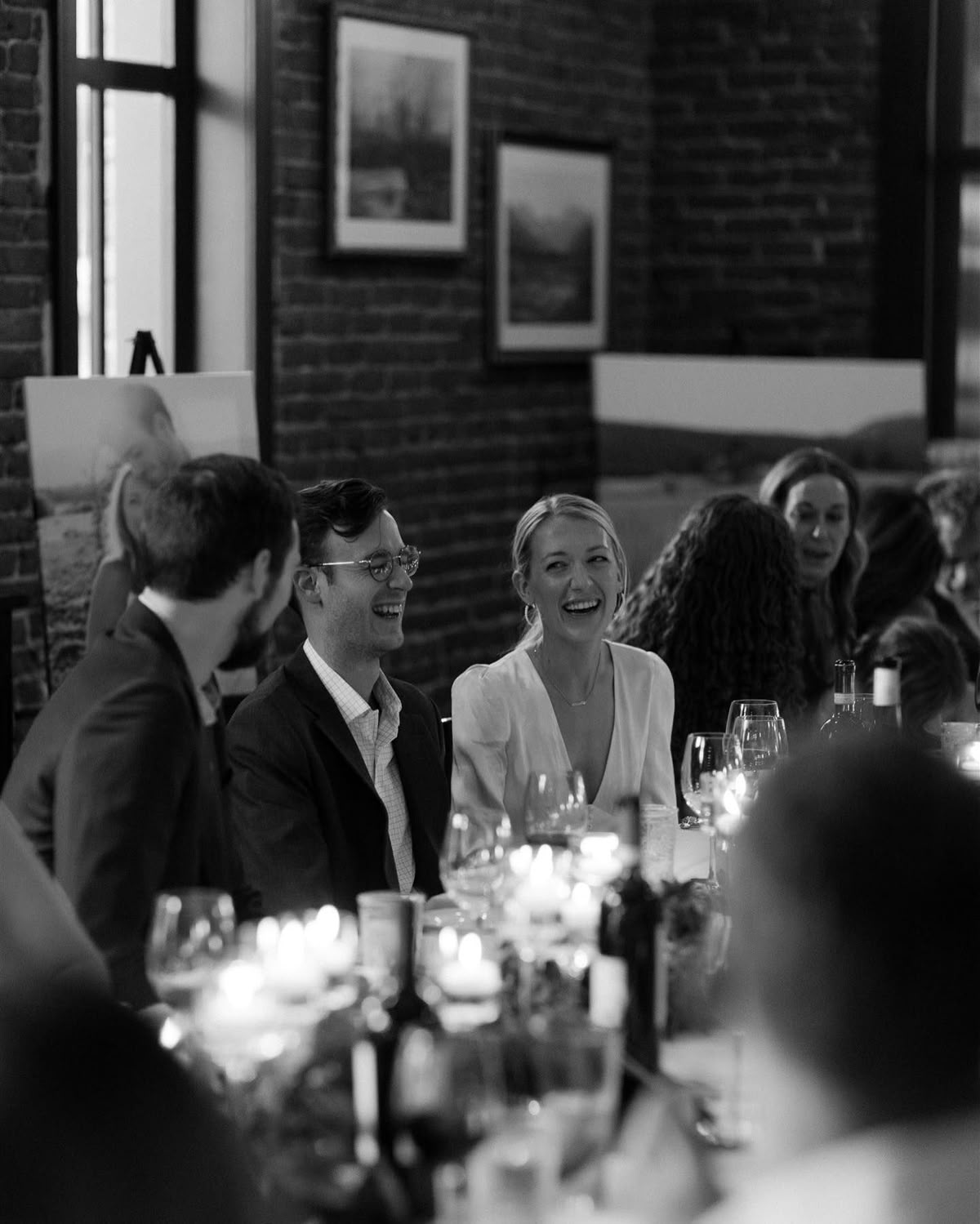 Black and white photo of wedding couple laughing at reception dinner table