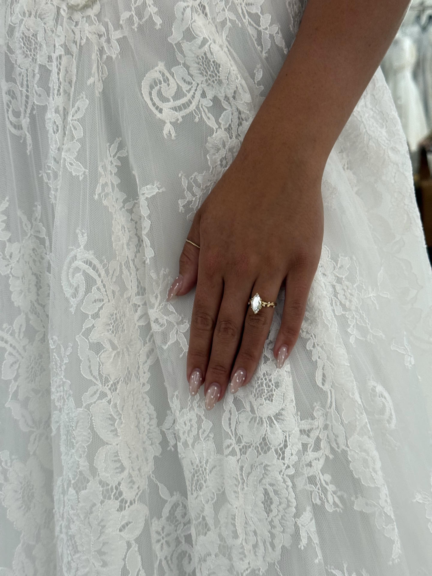 Bride's hand with engagement ring resting on lace wedding dress